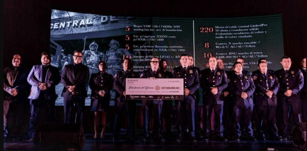 Integrantes del Heroico Cuerpo de Bomberos de Tijuana sosteniendo un cheque simbólico por 2,500,000 pesos en el escenario de la Borderless Gala, junto a organizadores y equipo técnico.