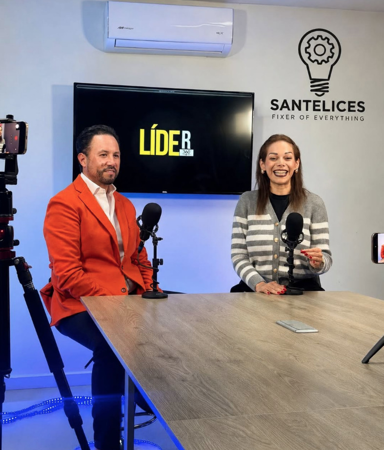 El empresario Marco Santelices, vistiendo un saco naranja brillante, sentado en un estudio de grabación junto a una conductora que sonríe. Al fondo se observa una pantalla con el logotipo de Líder 360 y en la pared el logo de Santelices Fixer of Everything.